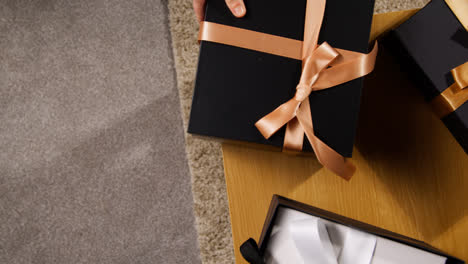 Overhead-Shot-Of-Man-Putting-Gift-Wrapped-Present-On-Table-At-Home